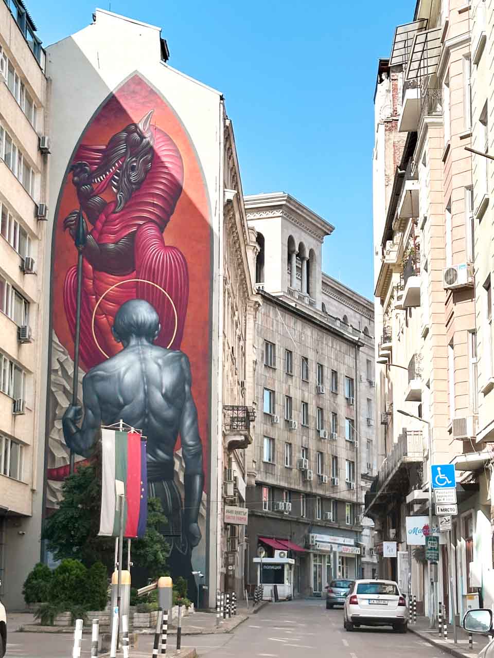 A large street art mural in Sofia showing a red horned creature towering over a grey human figure