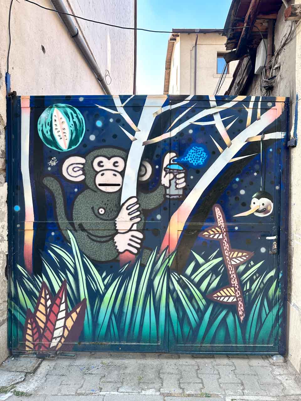 A colourful mural painted on metal gates in Sofia, showing a monkey among trees and plants, holding a spray can