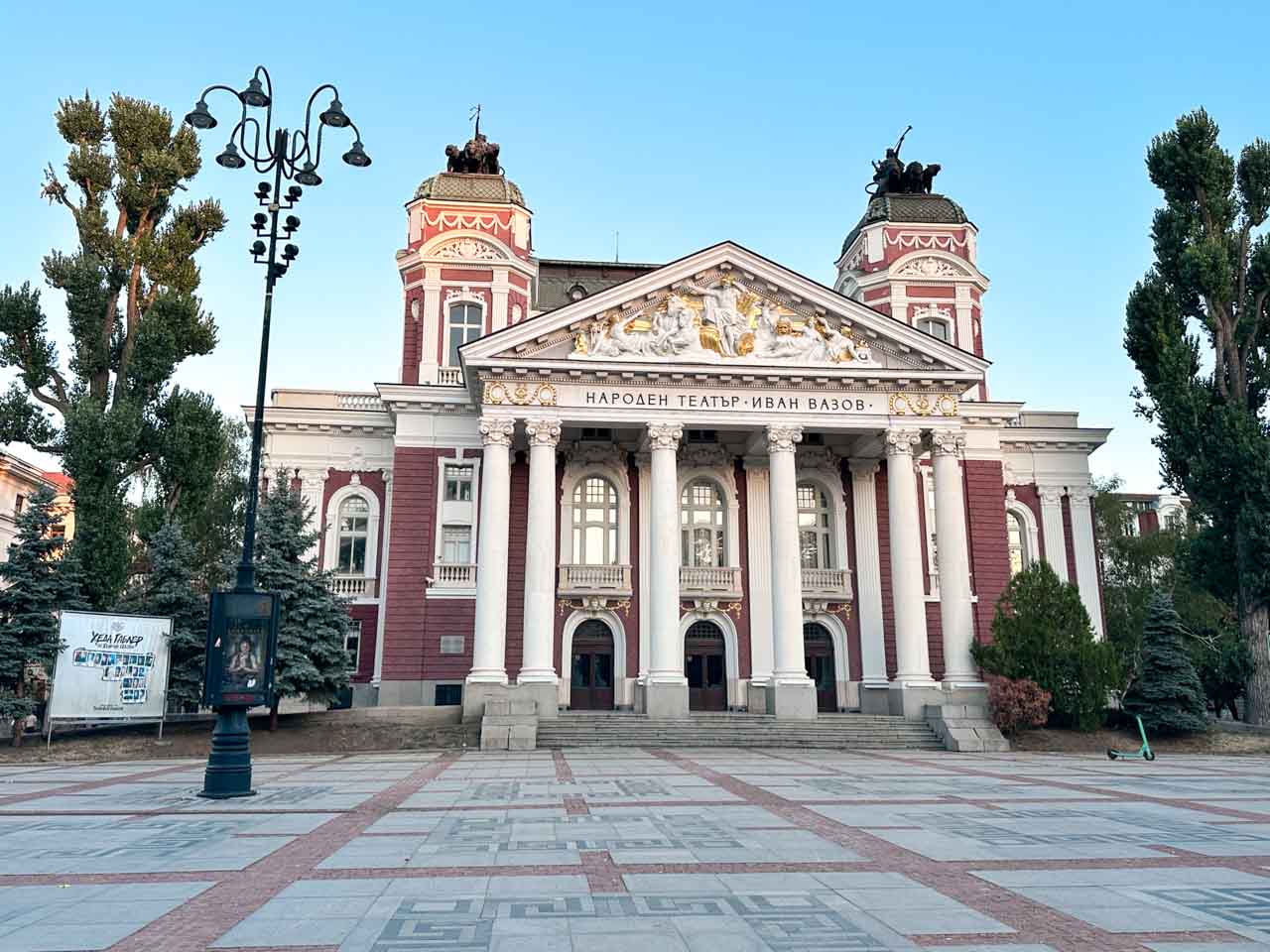 The red and white fa&ccedil;ade of the Ivan Vazov National Theatre in Sofia, with columns, sculptures, and a wide plaza