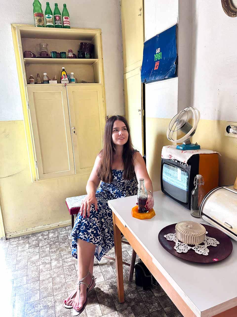 Woman in a blue and white dress sitting in a retro kitchen at the Red Flat museum in Sofia, Bulgaria
