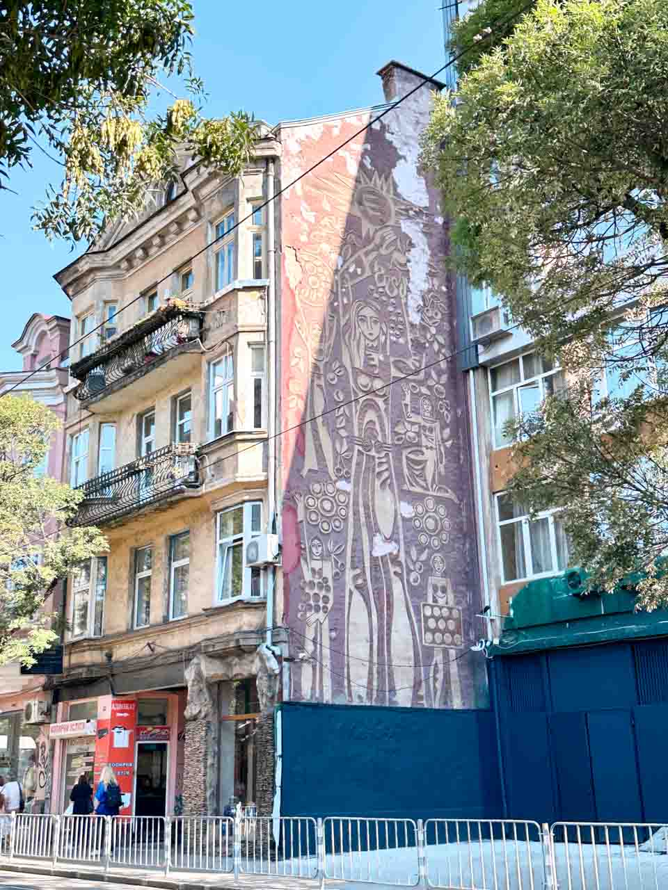 A large mural of a woman in a traditional Bulgarian dress surrounded by floral and folk-inspired patterns on a building in Sofia