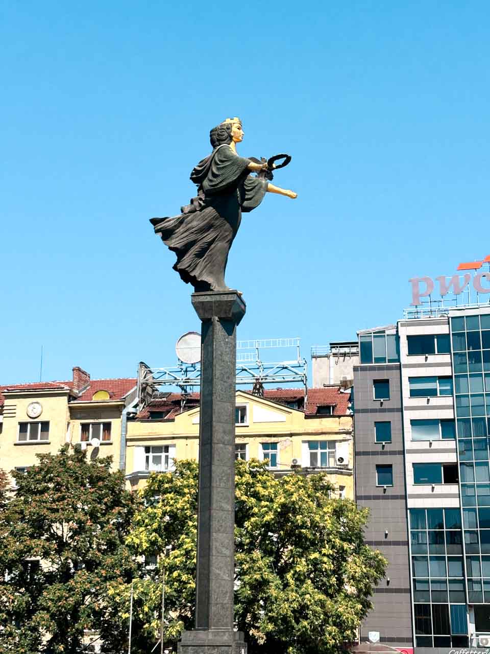 Statue of Saint Sofia on a tall column in central Sofia, with city buildings and trees in the background
