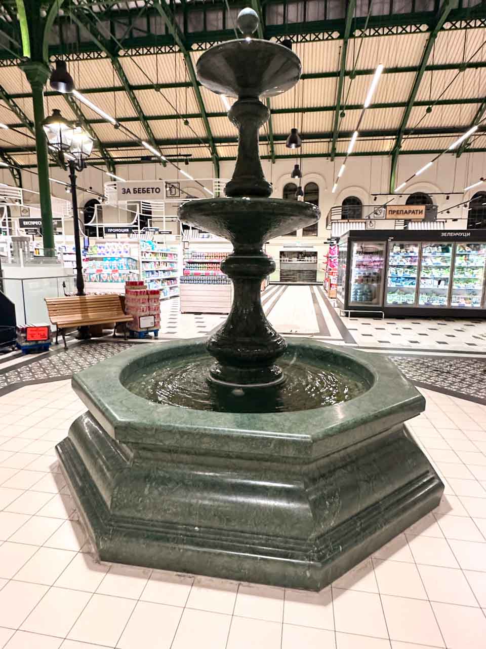Large stone fountain inside Sofia Central Market Hall, surrounded by supermarket aisles and refrigerated displays