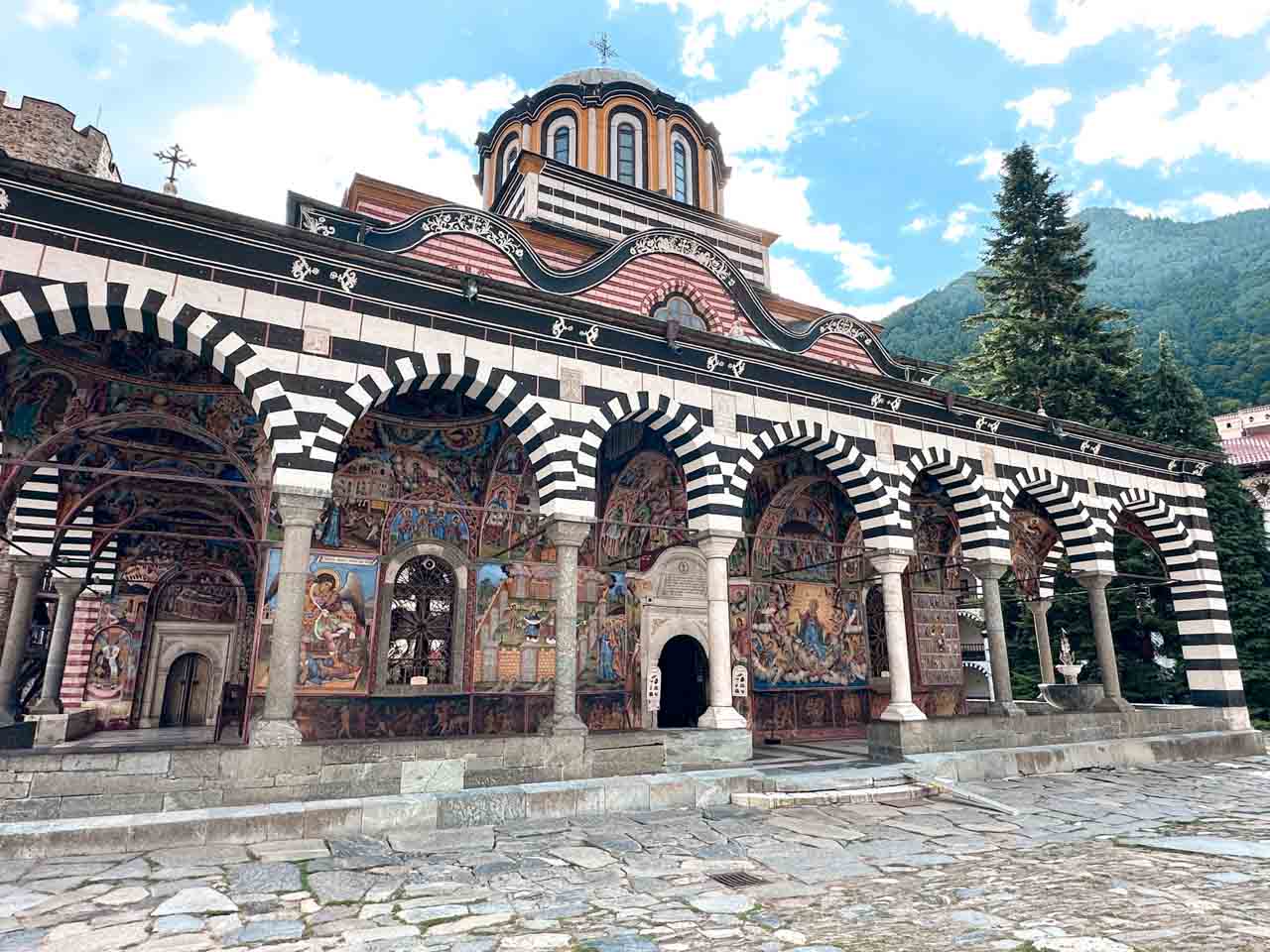 The church at Rila Monastery, with colourful frescoes covering the walls beneath its black-and-white striped arches