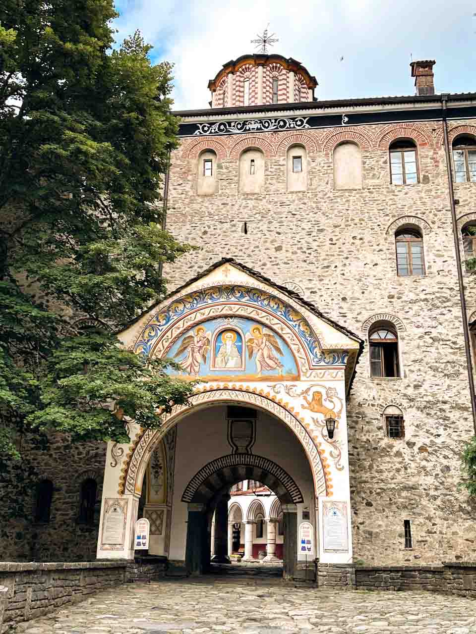 Arched entrance to Rila Monastery with colourful religious frescoes and a view into the courtyard beyond