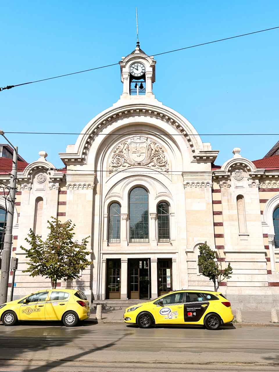 Central Market Hall in Sofia, with its arched fa&ccedil;ade and clock tower, and yellow taxis parked outside