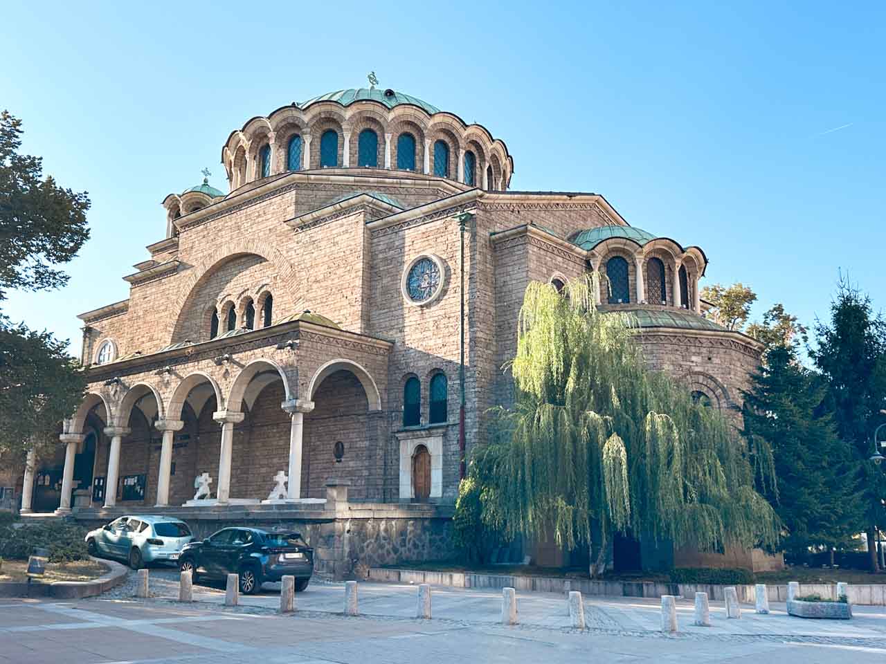 St Nedelya Church in Sofia, with its large domed roof, arched entrance, and a weeping willow tree beside it