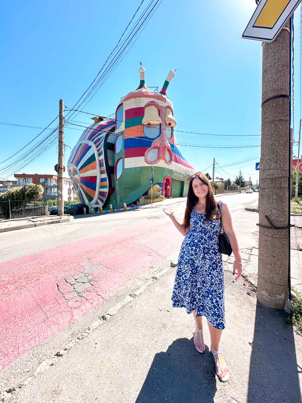 Woman in a blue and white dress posing in front of the colourful Snail House in Sofia, Bulgaria