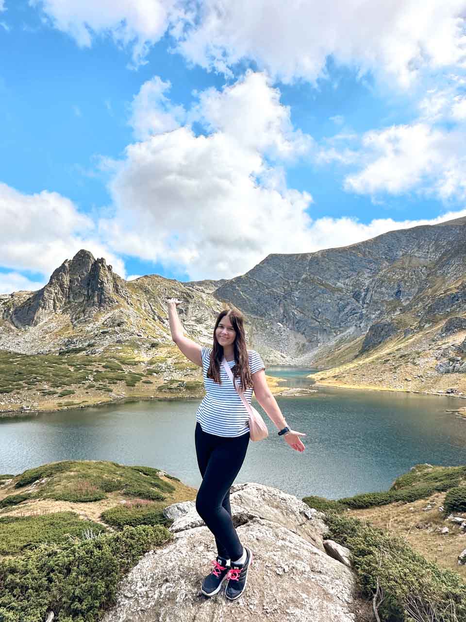 Woman in a striped t-shirt and black leggings posing beside one of the Seven Rila Lakes in Bulgaria
