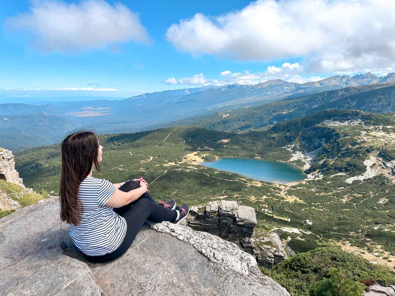 Woman sitting on a rocky viewpoint overlooking a lake in the Rila Mountains