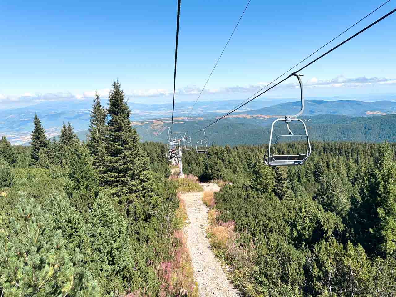 Chairlift descending over pine forest with sweeping views of the Rila Mountains and valley below