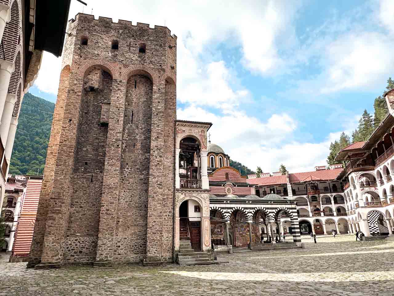 Historic stone tower, striped arches, and monastery buildings surrounding the courtyard of Rila Monastery