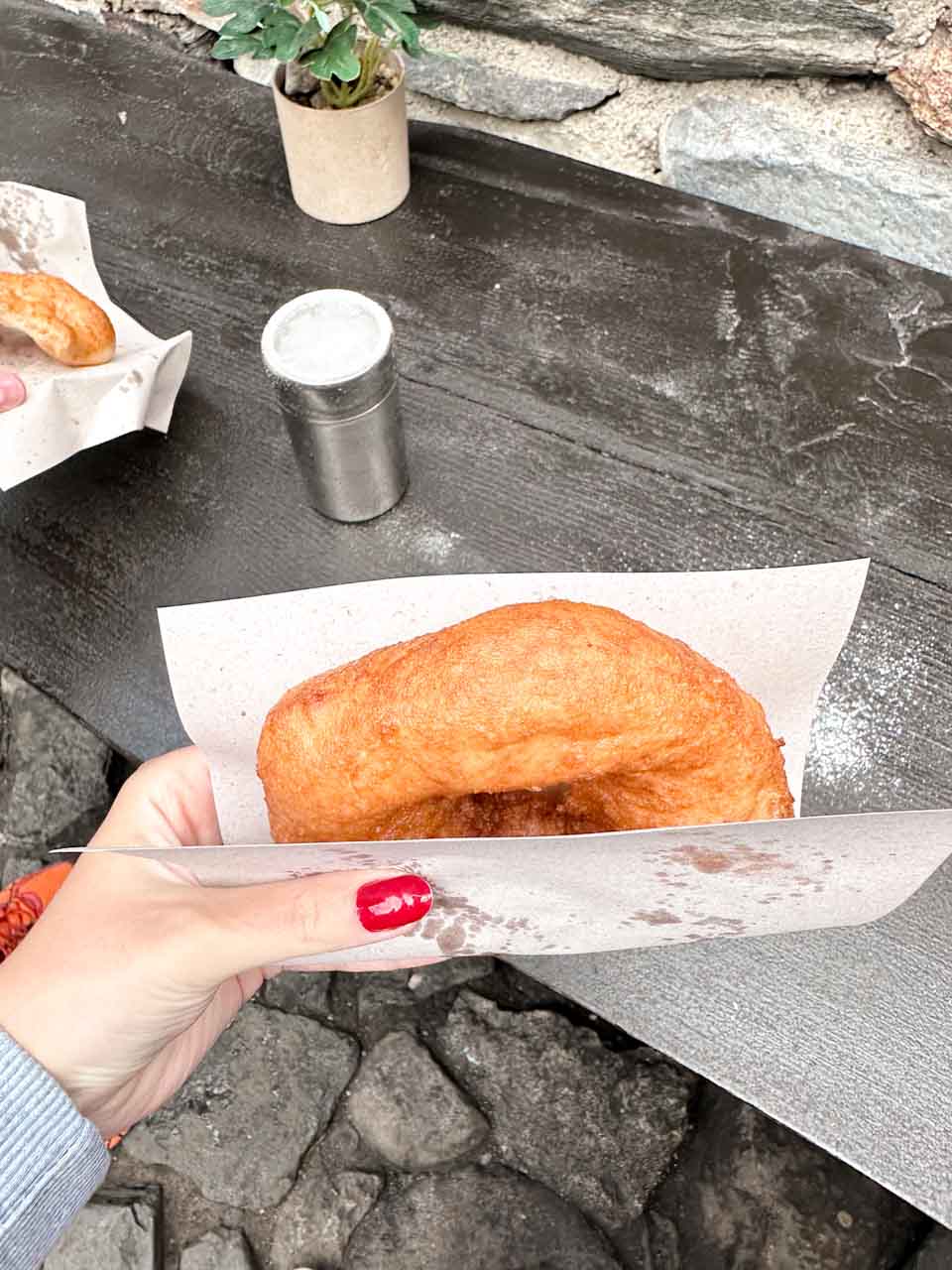 Traditional Bulgarian mekitsa held in one hand at Rila Monastery, with another pastry on the table
