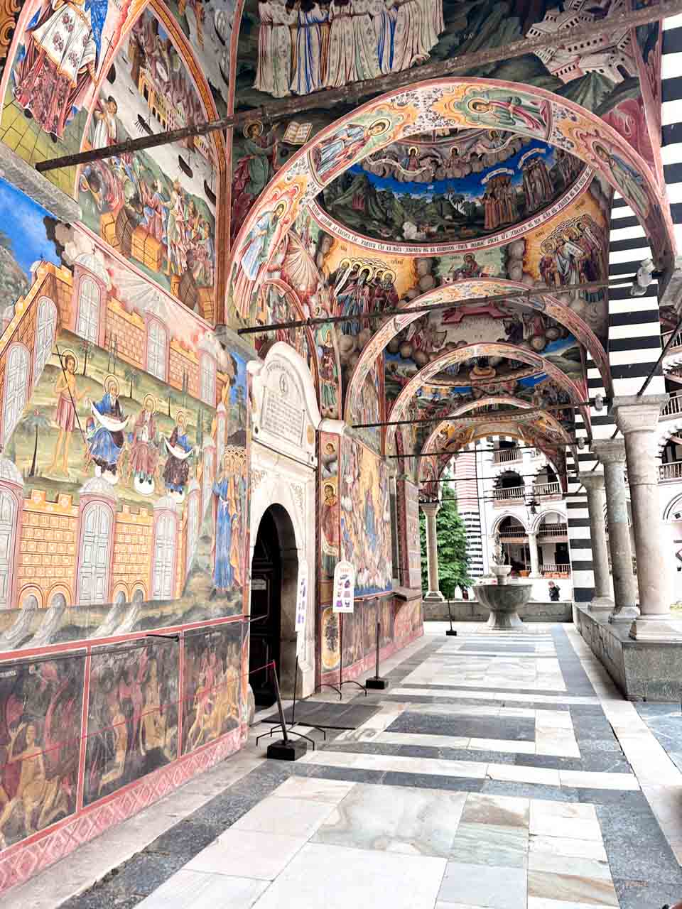 Colourful religious frescoes covering the arches and walls outside the church at Rila Monastery, Bulgaria