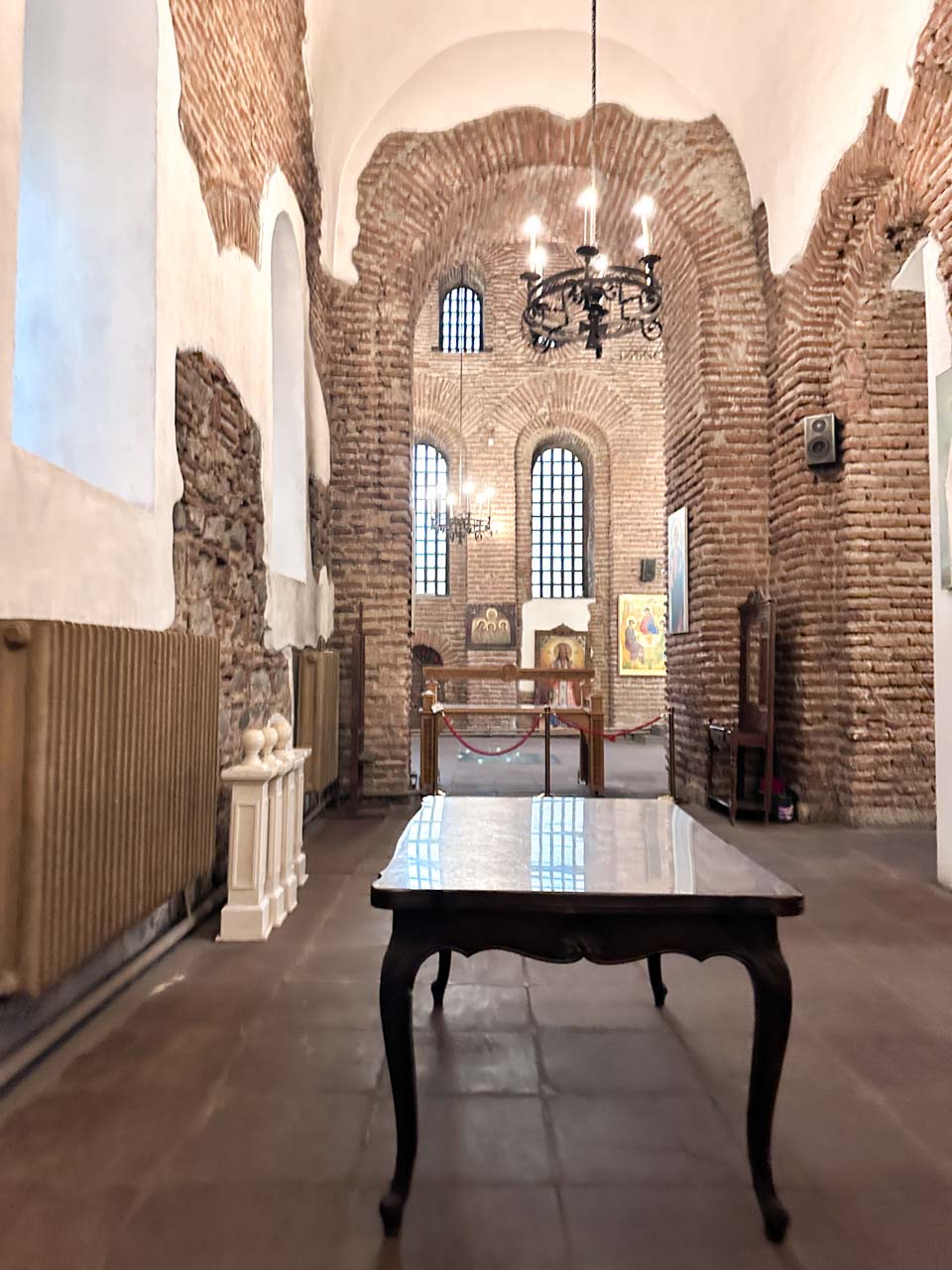 Interior of the Saint Sophia Church in Sofia with exposed brick walls, icons, and hanging chandeliers