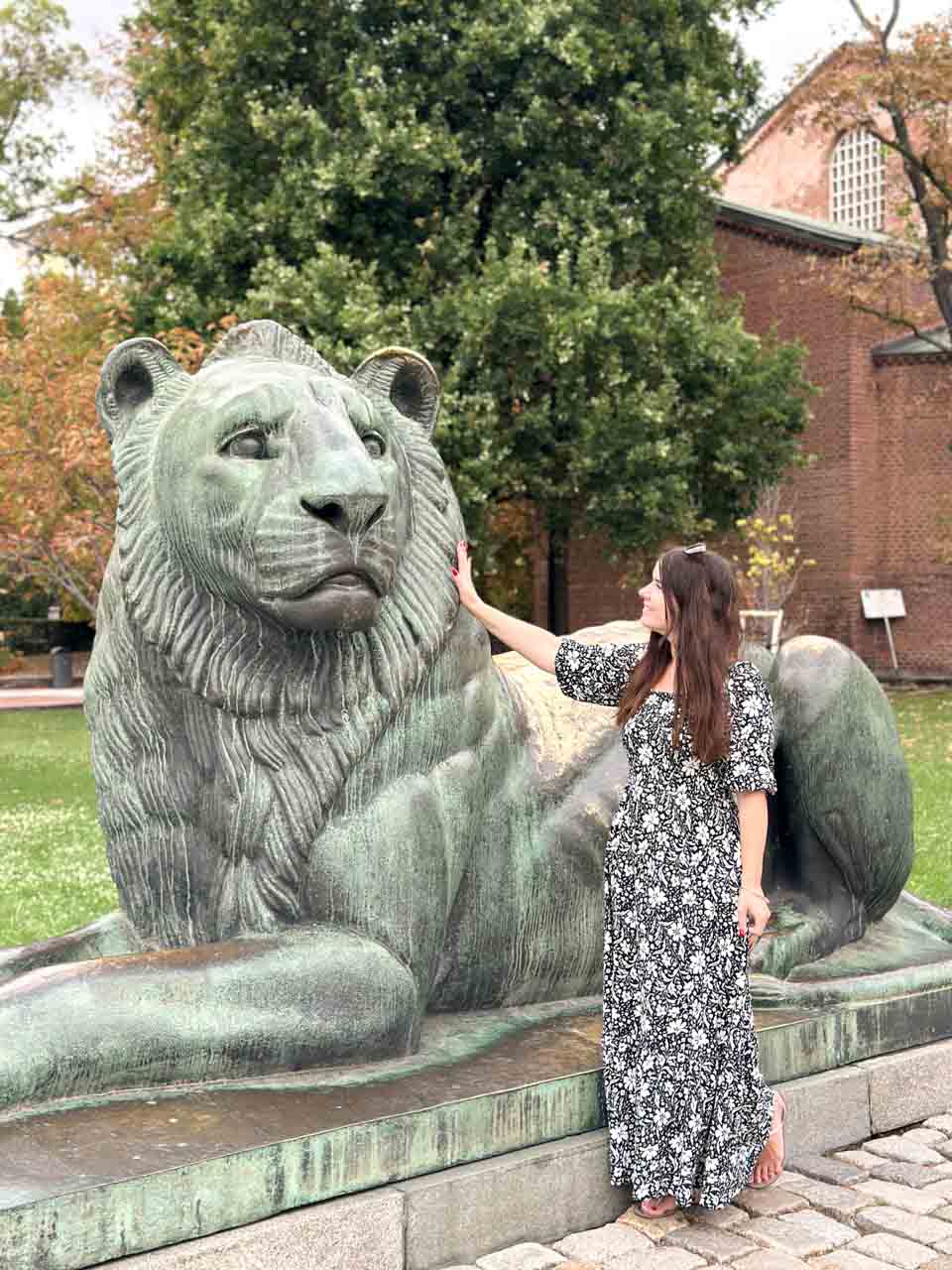 Woman standing beside a large bronze lion sculpture outside the Saint Sophia Church in Sofia