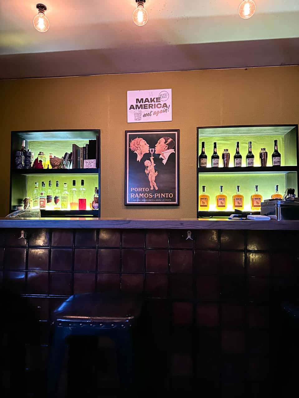 The dark tiled bar inside 5L Speakeasy Bar in Sofia, with illuminated shelves of bottles and a vintage poster on the wall