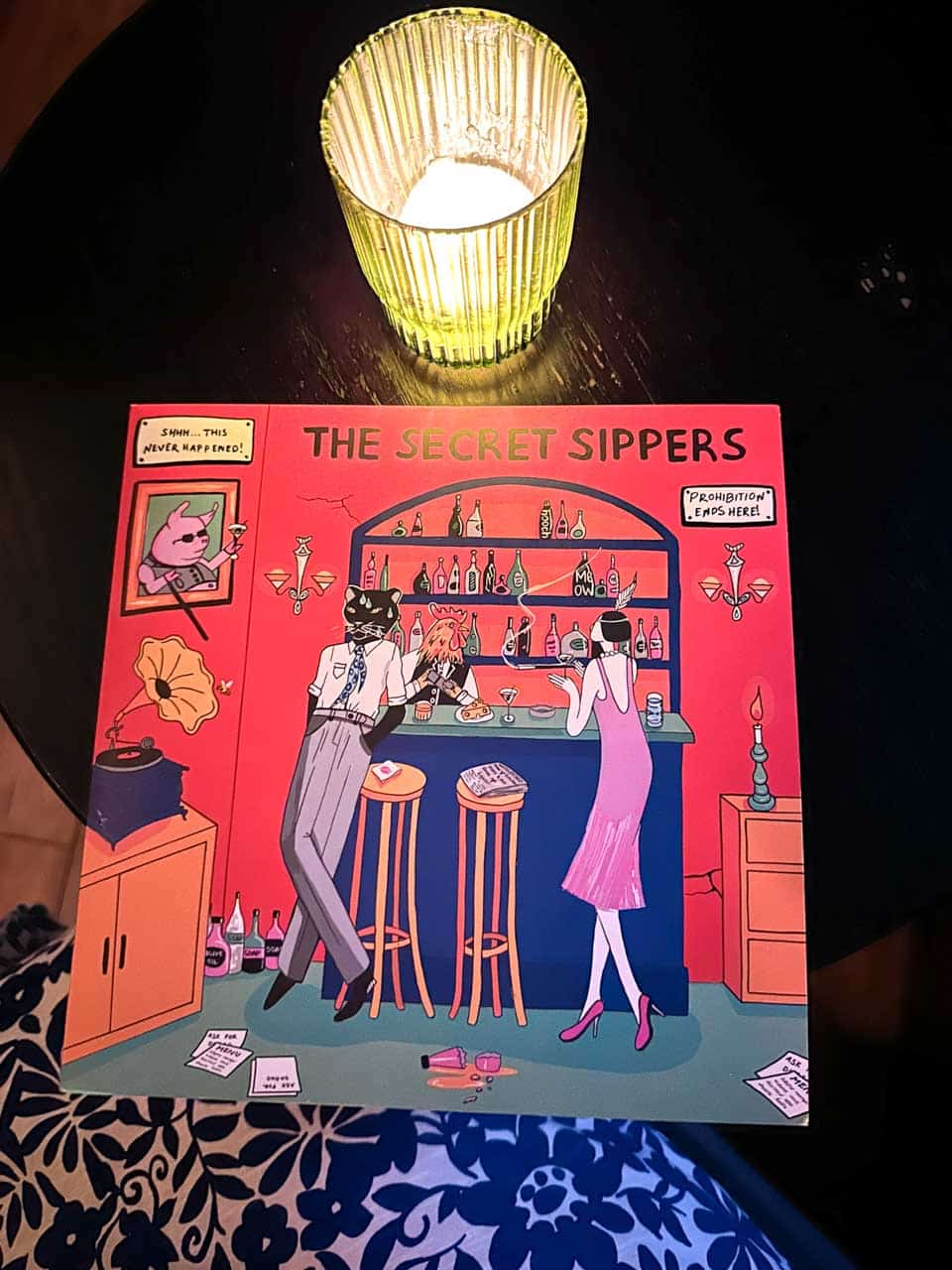 A colourful illustrated cocktail menu titled &ldquo;The Secret Sippers&rdquo; beside a candle at 5L Speakeasy Bar in Sofia, Bulgaria
