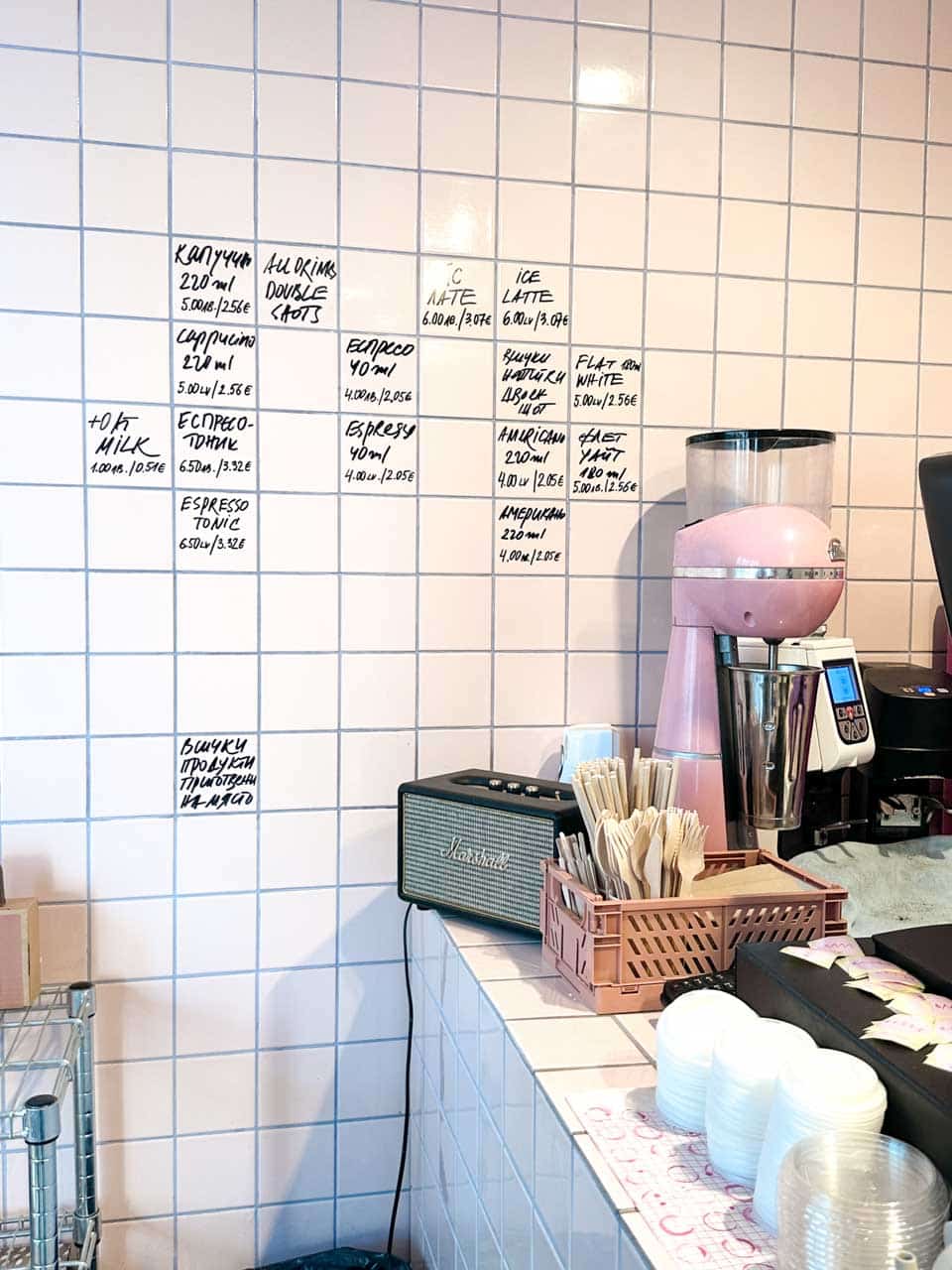 The minimalist tiled interior and handwritten coffee menu at &hlyab (&bread) in Sofia, with a pink coffee grinder on the counter