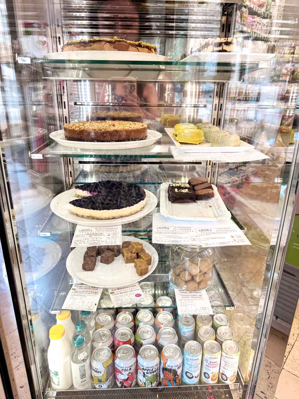 A display case filled with cakes, desserts, and drinks at Zoya in Sofia