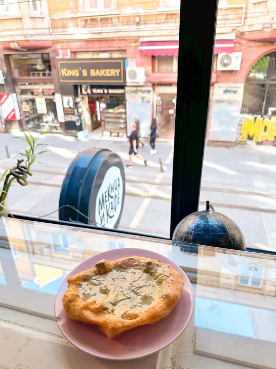 A freshly made mekitsa topped with a creamy pistachio spread, served by the window at Мекица и Кафе (Mekitsa & Coffee) in Sofia, Bulgaria