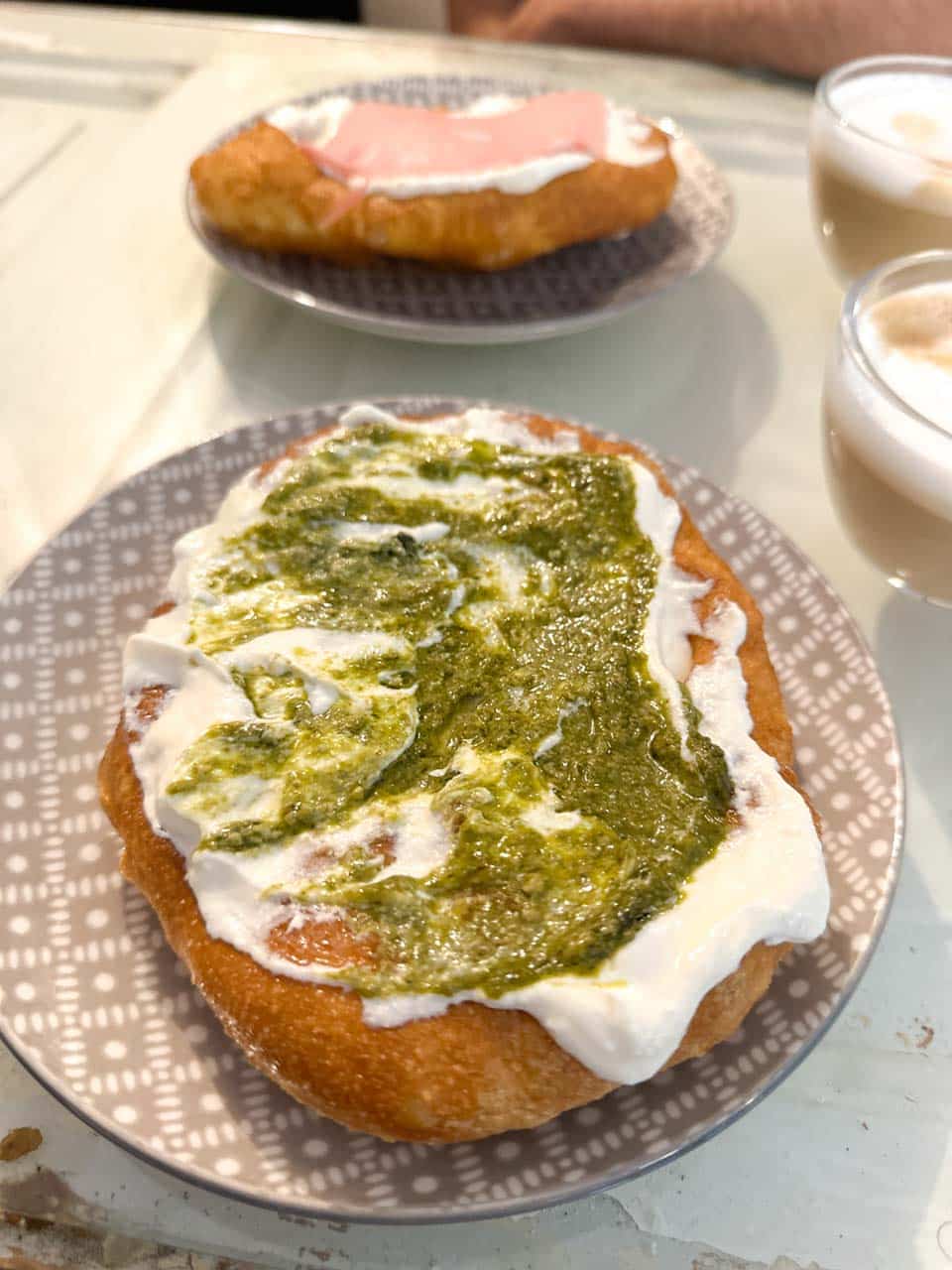 Fresh mekitsa topped with cream cheese and green pesto, with another topped with cream cheese and ham in the background at Мекица и Кафе (Mekitsa & Coffee) in Sofia