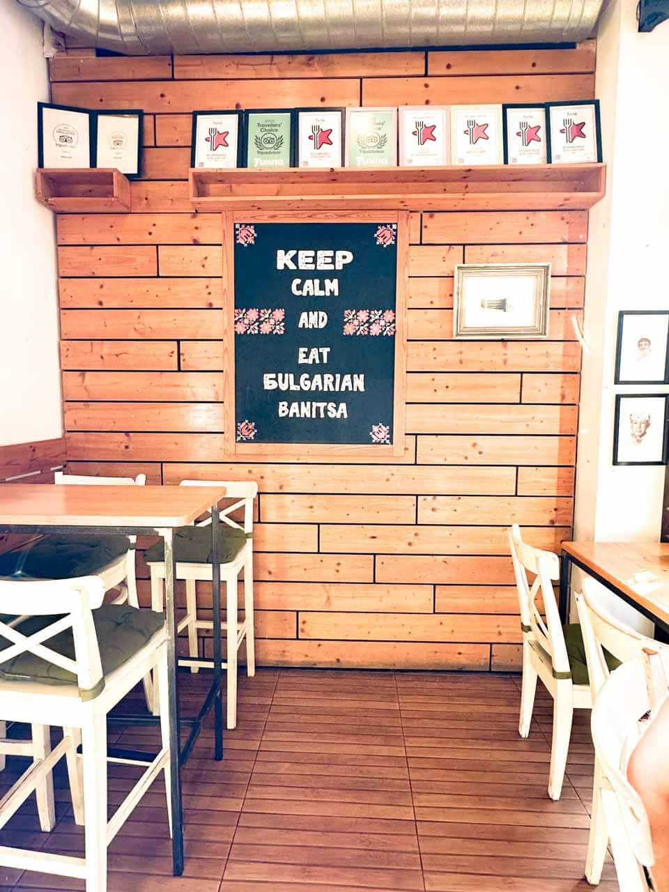 The cosy interior of Furna bakery in Sofia, with wooden walls, simple tables and chairs, and a sign reading &ldquo;Keep calm and eat Bulgarian banitsa&rdquo;