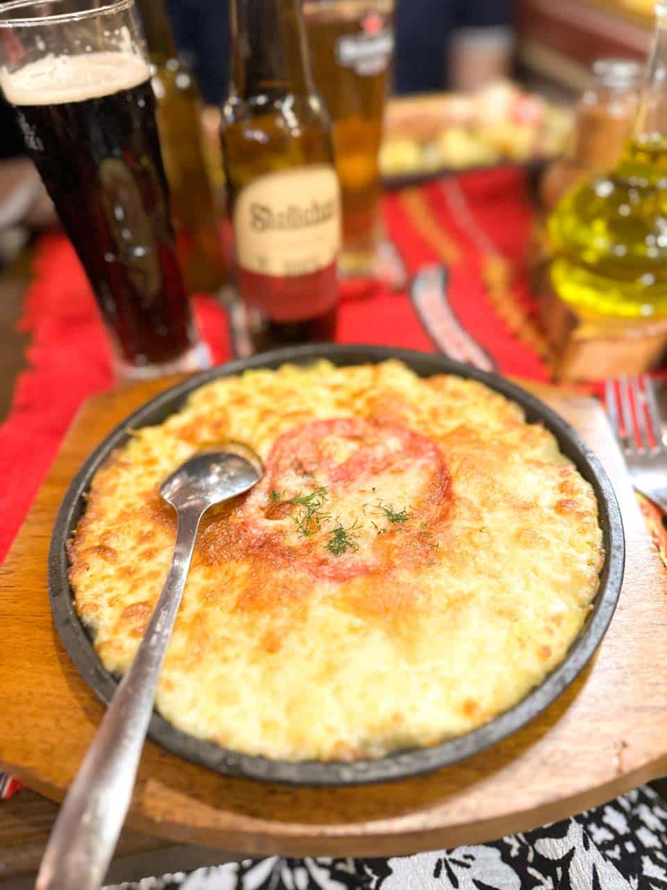 Traditional Bulgarian patatnik topped with melted cheese and tomato at Hadjidraganov's Cellars Restaurant in Sofia, Bulgaria