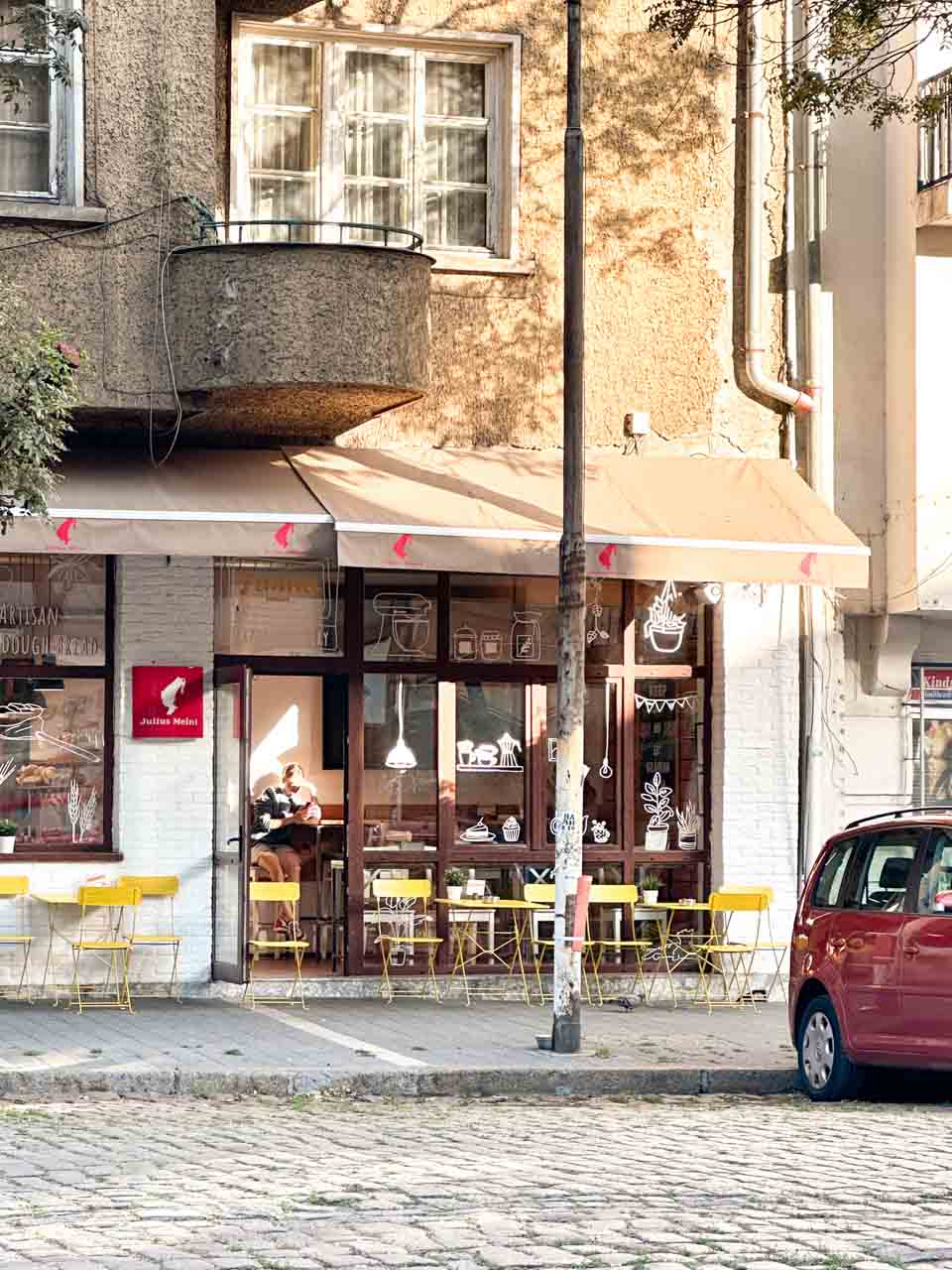 The exterior of Furna bakery in Sofia, with yellow tables and chairs outside