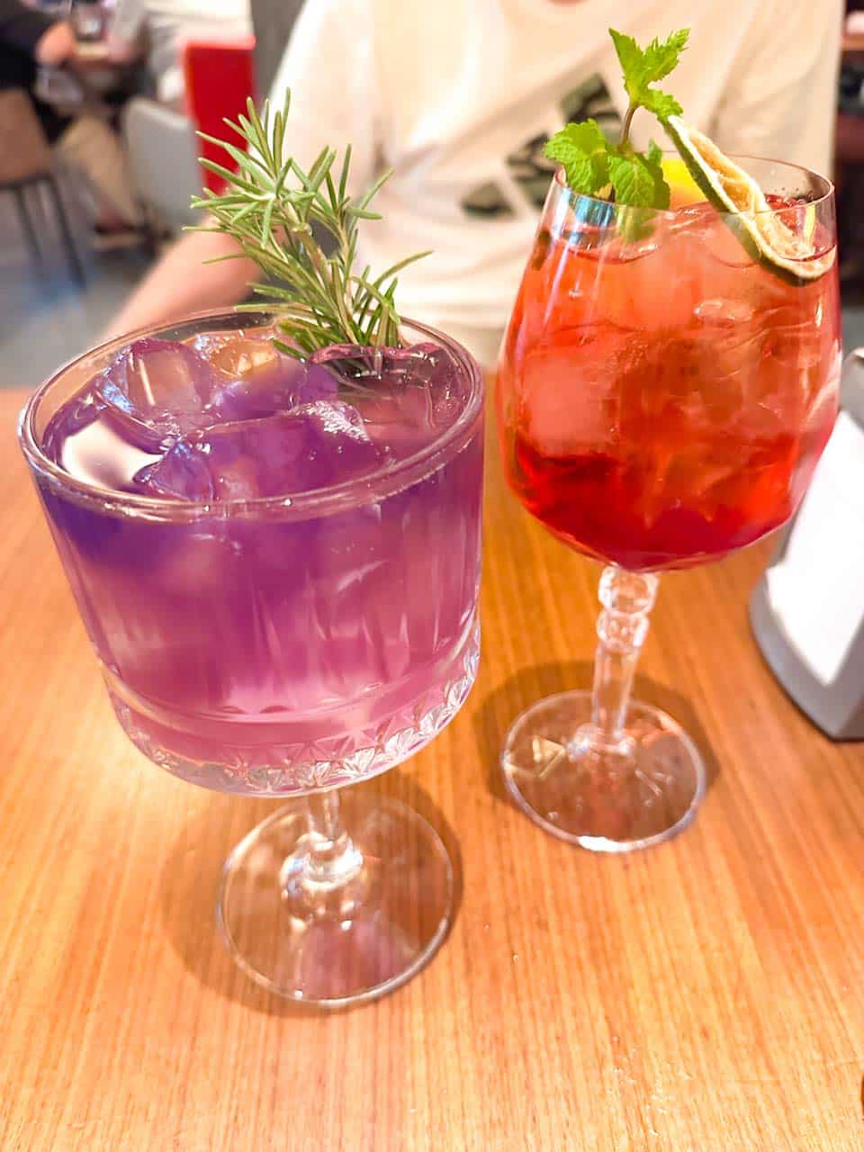 Purple and red cocktails with ice, rosemary, mint, and dried citrus garnishes at Happy Bar & Grill in Sofia, Bulgaria