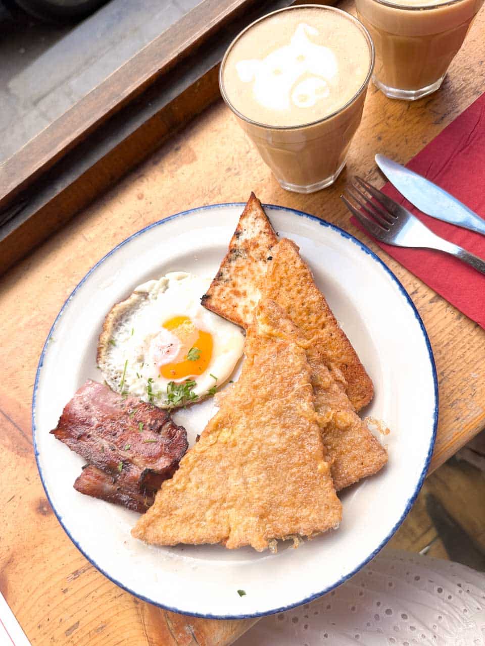 Egg-coated toast served with a fried egg and bacon, with a cup of coffee at Rainbow Factory in Sofia