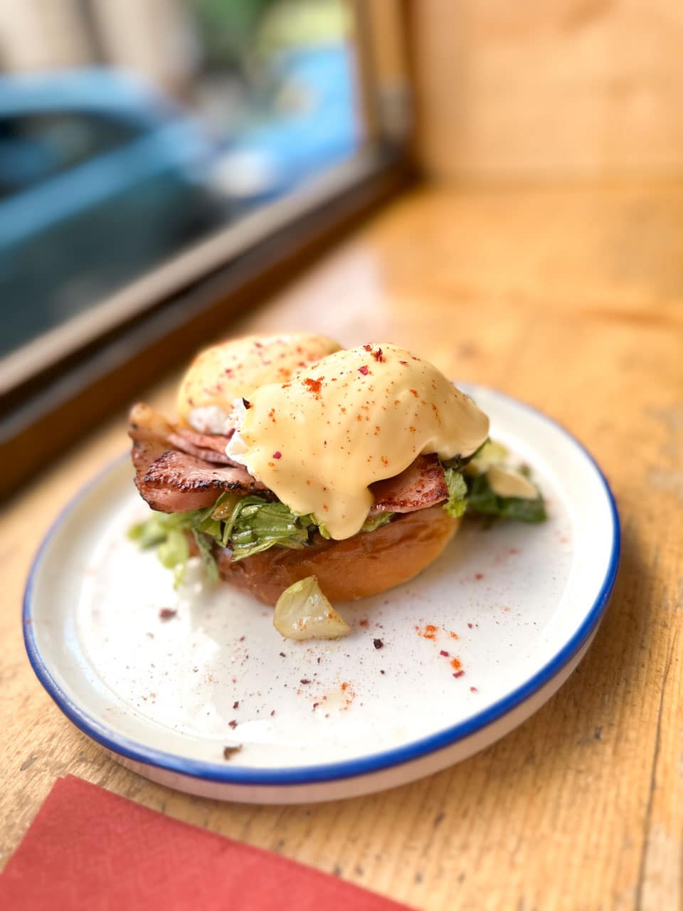 Eggs Benedict with bacon, greens, and hollandaise sauce on a toasted bun at Rainbow Factory in Sofia