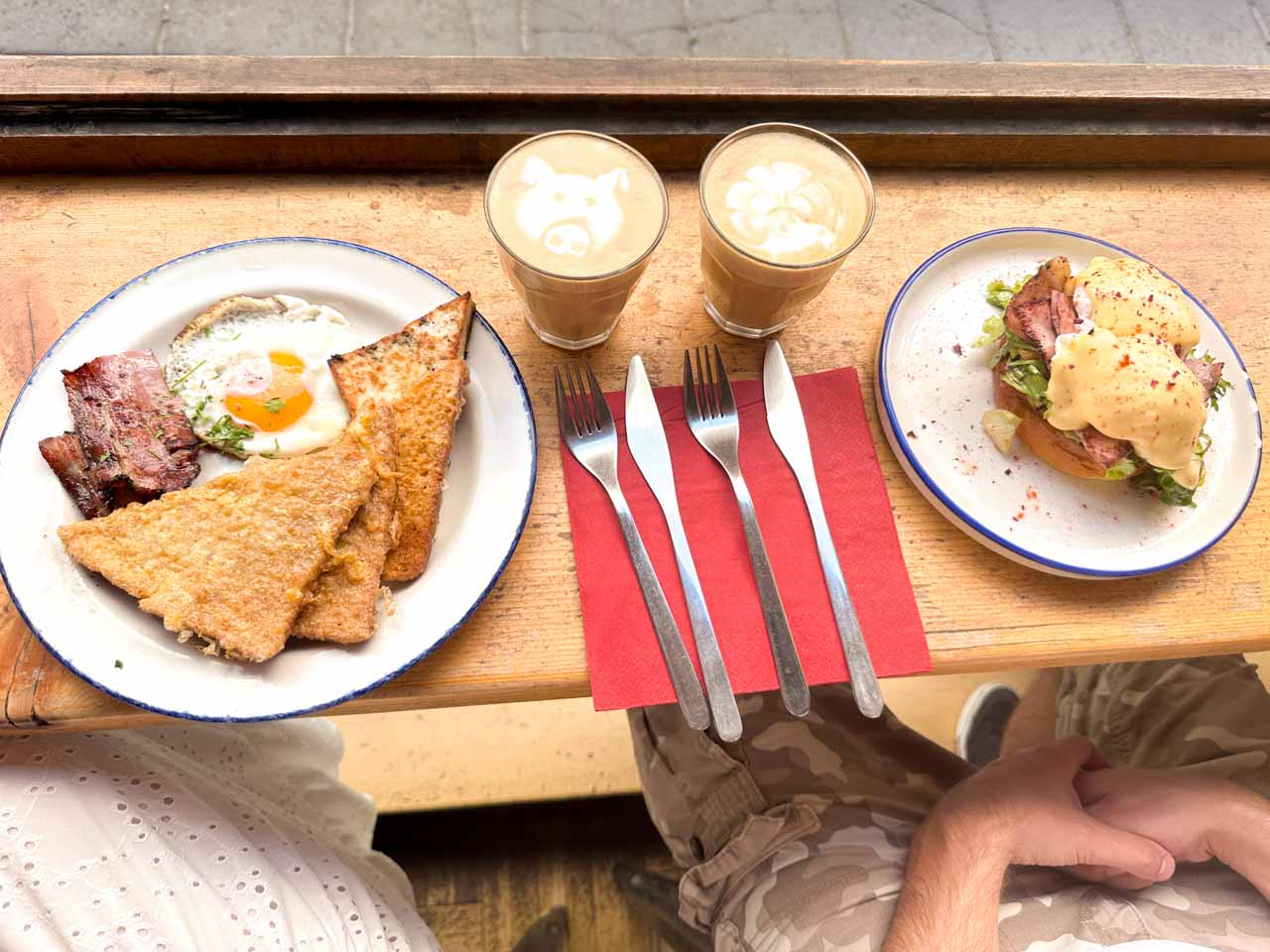 Breakfast at Rainbow Factory with egg-coated toast, bacon, and a fried egg; Eggs Benedict; and two coffees with latte art