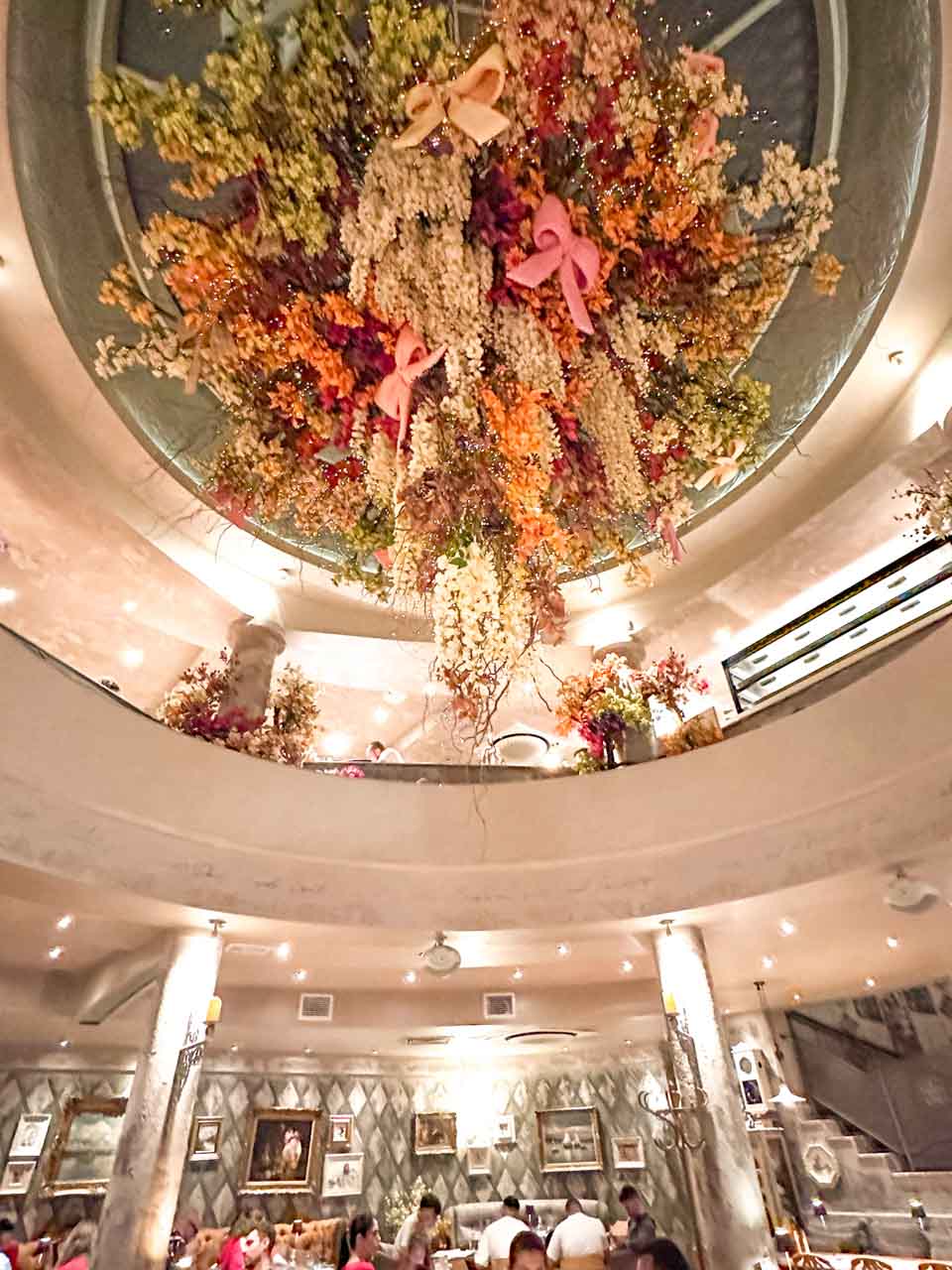 Elegant interior of Shtastlivetsa Restaurant in Sofia with a large hanging floral installation, framed artwork, and two levels of dining tables