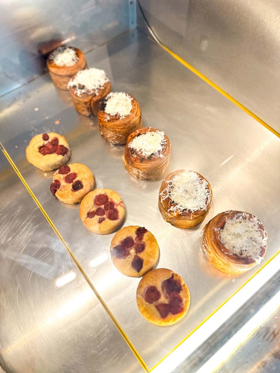 Raspberry cakes and flaky pastries topped with grated cheese in the display case at &hlyab (&bread) in Sofia